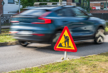 Blurred car passing road construction warning sign.