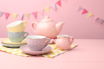 Beautiful ceramic tea set for children on wooden table against pink background with party flags, closeup. Space for text