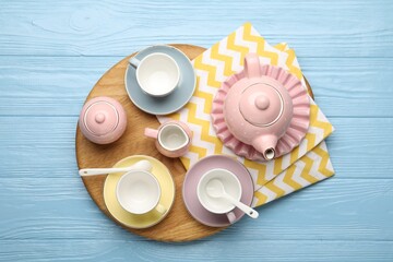 Beautiful ceramic tea set for children and napkin on light blue wooden table, top view