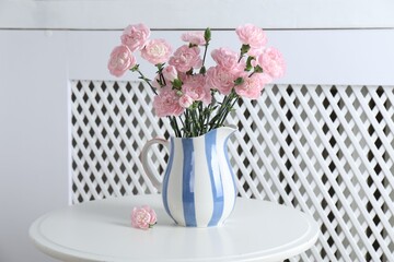 Beautiful carnation flowers in jug on white table indoors