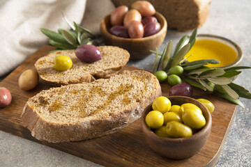 Mediterranean snack with mixed olives, olive oil, and rustic bread on wooden board.