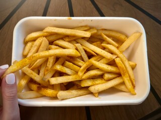 Golden french fries with black pepper seasoning in white takeout container