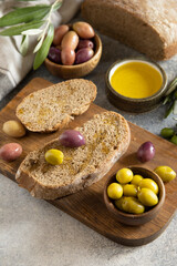 Mediterranean snack with mixed olives, olive oil, and rustic bread on wooden board. Copy space.