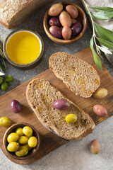 Mediterranean snack with mixed olives, olive oil, and rustic bread on wooden board.