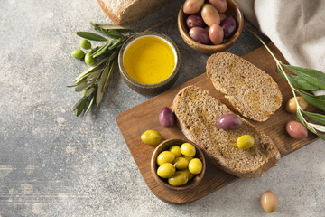 Mediterranean snack with mixed olives, olive oil, and rustic bread on wooden board.