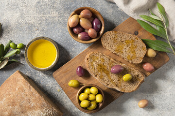 Mediterranean snack with mixed olives, olive oil, and rustic bread on wooden board. Top view flat lay background.