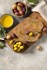 Mediterranean snack with mixed olives, olive oil, and rustic bread on wooden board.