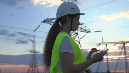 An adult woman electrician is working with tablet modern technologies next to power plant, setting...