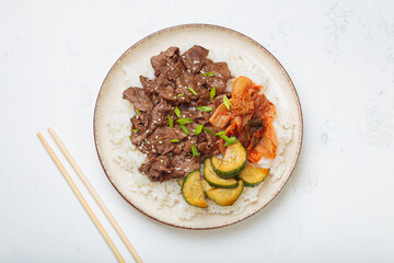 Beef bulgogi bowl dish with rice, roasted meat slices, kimchi and marinated cucumber on white background top view, traditional dish of Korea