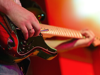 Close-up of a person's hand playing a red electric guitar on a stage