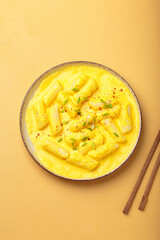 Delicious korean tteokbokki rice cakes served in a creamy cheese sauce, topped with green onion slices, presented in a bowl with chopsticks, authentic food of Korea