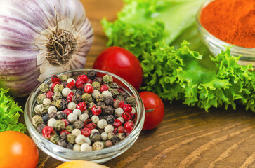 Mix of peppers among vegetables of green salad and cherry tomatoes, garlic on wooden board