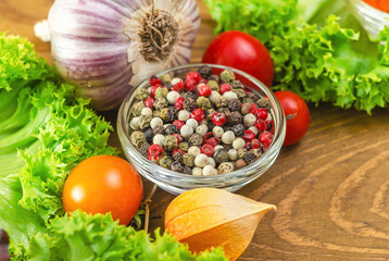 Mix of peppers among vegetables of green salad and cherry tomatoes, garlic, physalis on wooden board