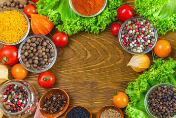 Aromatic spices and cherry tomatoes, garlic, physalis, salad greens and spoons on wooden background.