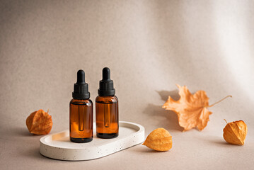Cosmetic serum in brown glass dropper bottles in sunlight on a beige background with dried autumn plants. Selective focus, copy space.