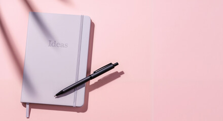 Minimalist notebook with "Ideas" text and a pen on a pink background with palm leaf shadows.
