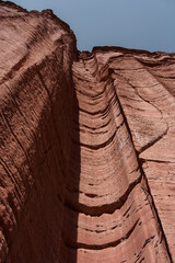 Tall red rock cliff with layered geological formations under clear sky
