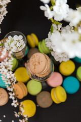many colored macaroons on a black background with white apple blossom