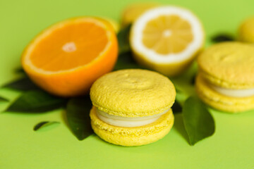 Lemon-flavored macaroons lie on a green background with citrus fruits and leaves
