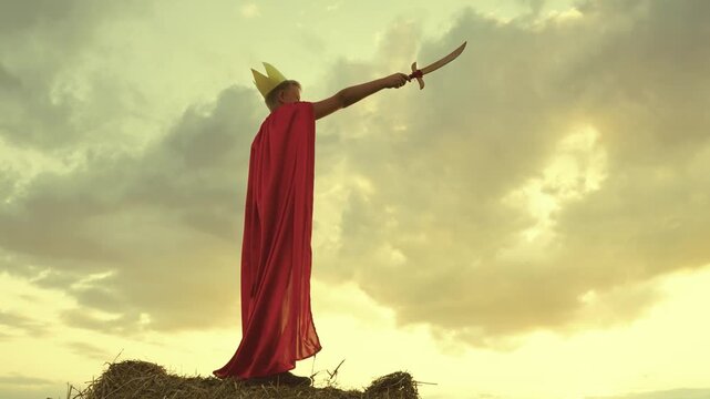 child superhero game sunset. red cape childish fantasy. countryside. golden crown head kid. achieve victory success. schoolboy plays sword. happy child superman red raincoat nature. concept happy