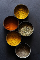 Assorted spices in round containers on dark background