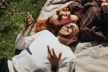 A cheerful couple laying together on a blanket outdoors, enjoying sunny weather.