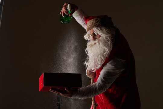 Santa Claus spraying magic over red gift box on dark background for Christmas ads - Powered by Adobe