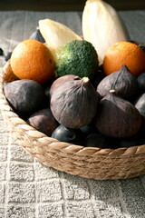 Fototapeta premium A close-up shot of a wicker basket overflowing with a diverse selection of fresh, ripe fruits and vegetables, including figs, oranges, plums, and broccoli, under natural light.