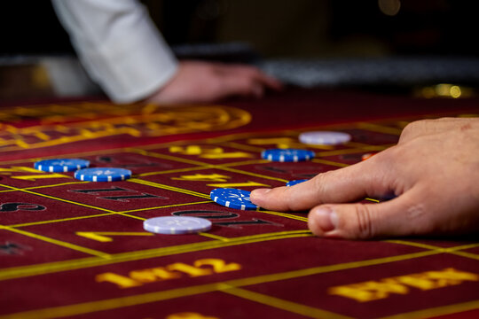Man playing at the roulette table. A close-up vibrant image of multicolored casino table with roulette in motion, with casino chips. the hand of croupier.