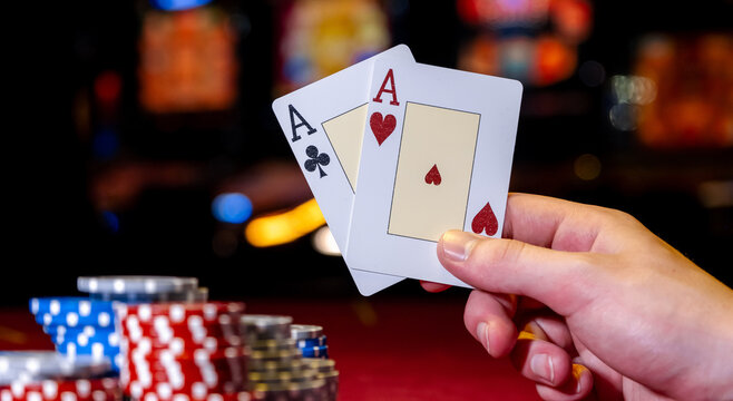 Player opens playing cards with one pair or two aces on red poker table. Close-up of playing chips and hand with cards on table in club or casino.
