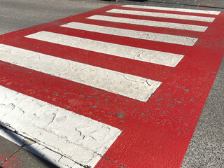 Weathered red and white pedestrian crosswalk on asphalt street surface