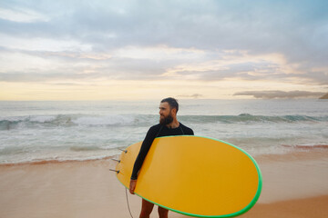 Young  bearded man with surfboard standing near a beach. Man with surfing board outdoors on a summer day.