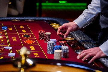 Croupier behind gambling table in a casino. Roulette wheel and croupier hand. A player in a casino,...