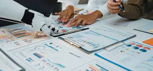 A collaborative office scene featuring human hands working alongside a robotic arm, highlighting data analysis and innovative technology in a productive environment.Noogenesis