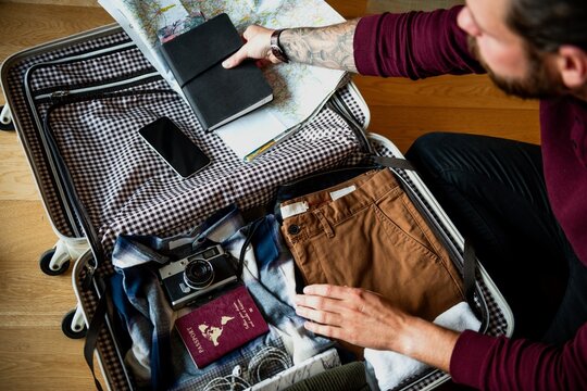 Man packing suitcase with clothes, map, and camera. Travel essentials include a map, camera, and clothes. Preparing for a trip with a suitcase and travel items. Man getting ready to travel. - Powered by Adobe