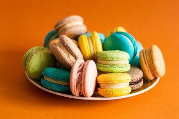 Large round plate full of colorful macaroons on an orange solid background