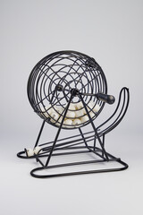 Bingo lottery ball dispenser, made of black metal mesh and crank handle. White background in...