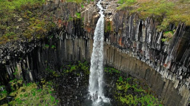 Svartifoss waterfall Skaftafell Iceland aerial close-up. 4K cinematic drone footage shows water flowing between basalt cliffs into lush green valley.