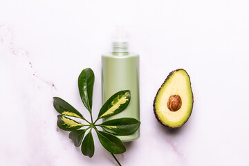 Skin care organic products such as shower gel or cream, or lotion and hand made soap with avocado oil on white marble background decorated with fresh avocado slices and palm leaves.