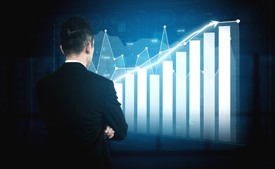 A businessman stands in a dark office, observing a growth chart represented with data visualization...