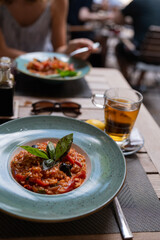 Close-up of a plate with tomato risotto, olives and basil on a rustic wooden table. Tea and lemon on the side. Outdoor dining in a cozy café setting, warm and relaxed summer vibe