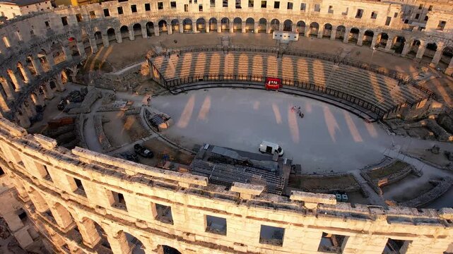 4K aerial footage showing the interior of Pula Arena, one of the best-preserved Roman amphitheaters in the world. Captured at golden hour, highlighting ancient architecture, stone arches, and historic