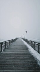 Obraz premium The winter pier perspective offers a glimpse into a snowy, foggy day at the lakefront. The mist softens the landscape, while snow blankets the ground and pier, creating a tranquil scene filled with