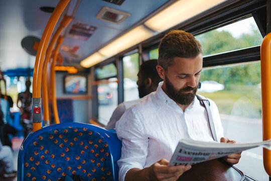 Man sitting in bus and reading newspapers, travelling to work.