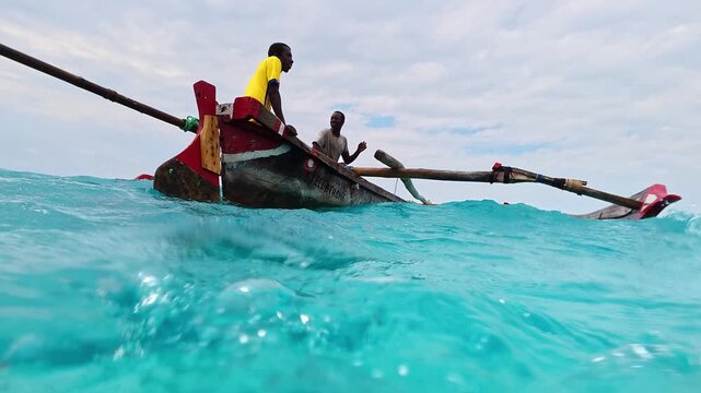 African man sailor in traditional wooden fishing boat in crystal clear turquoise water near Nungwi beach in Zanzibar. African tropical island tourism destination in Tanzania. 