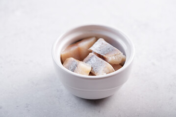 Herring slices in a white bowl on a white background