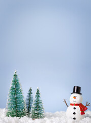 Christmas greeting card. Snowman and new year trees on snow over blue paper background with copy space