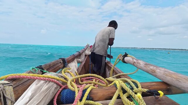 African man sailor on traditional wooden boat sail called dhow, near Nungwi beach in Zanzibar. African tropical island, tourism destination in Tanzania. 