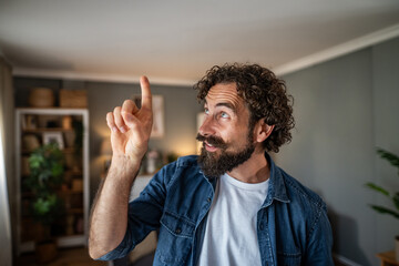 Happy bearded man pointing upward with idea expression indoors © Migma_Agency