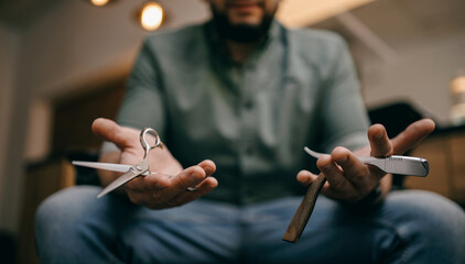 Male barber holding scissors and straight razor in barbershop setting
